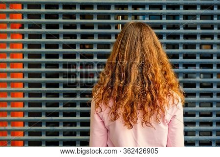 The Back View Of A Girl Standing In Front Of Metal Grid Wall