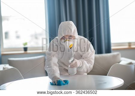 Woman In White Workwear And Protective Gloves Cleaning The Table Surface