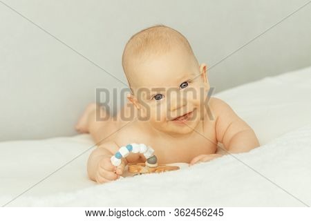 Adorable Little Baby Boy With Rattle On The Sofa Theething And Chewing Theethers