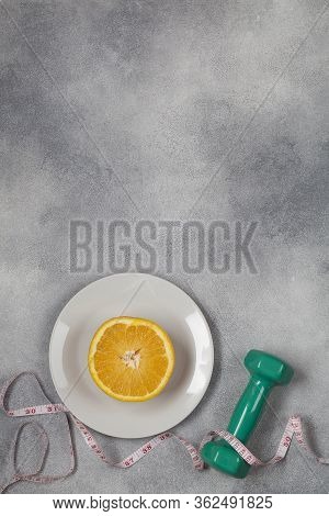 Green Dumbbell With Measurement And Plate With Cut Orange On Blue Background