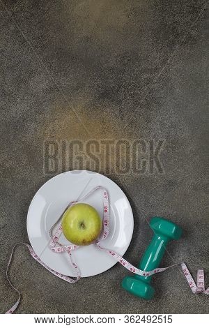 Green Dumbbell With Measurement And Plate With Apple On Dark Background