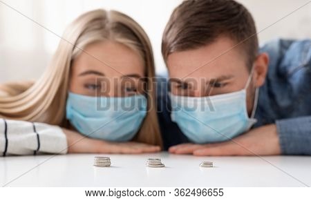 Coronacrisis In Family. Sad Man And Woman In Protective Masks Counting Last Money Savings At Home, C