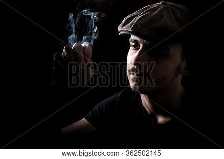 Portrait Of Cute Young Guy With Moustache And A Hat On Black, Dark Background Smoking A Cigarette.