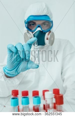 COVID-19 or 2019-nCoV. Doctor microbiologist scientist in a protective PPE suit shows the ampoule with a vaccine against coronavirus. Vaccination.