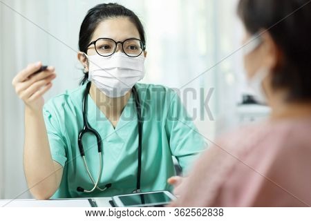 Asian Female Doctor In Green Uniform Wear Glasses And Surgical Mask Talking, Consulting And Giving A