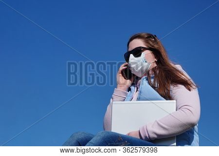 A Business Woman Speaks On Phone On Street In Medical Mask During Coronavirus Pandemic Against Backg