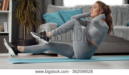 Athletic Young Lady Doing Abs Exercises, Sit-ups, Leg Raising, Twisting Staying Indoors