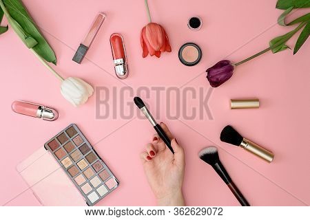 Girl Holds Makeup Brush Set Of Cosmetics And Flowers On Pink Background