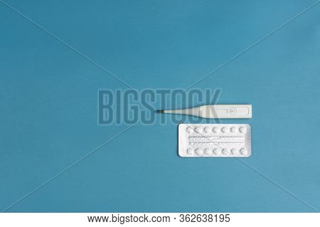 Electronic Thermometer With A Flexible Tip And A Blister Of Square Tablets On A Blue Background