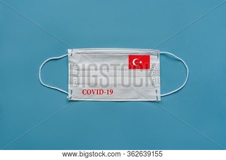 Medical Mask With The Flag Of Turkey And The Inscription Covid-19 On A Blue Background