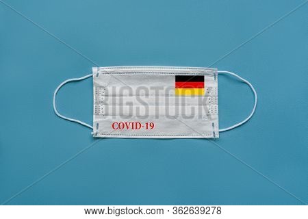 Medical Mask With The Flag Of Germany And The Inscription Covid-19 On A Blue Background