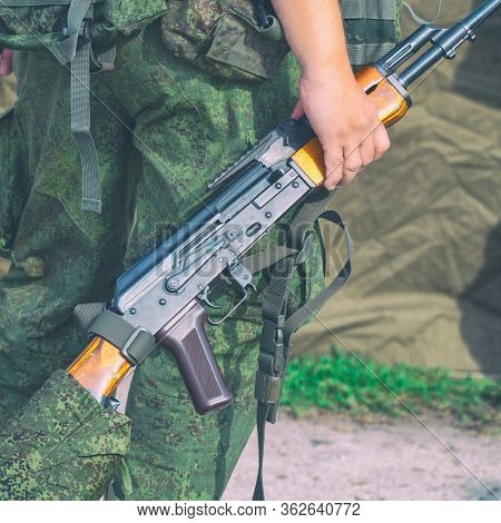 A Soldier In Camouflage Uniform Holds In His Hands A Kalashnikov Machine Gun Without A Magazine.