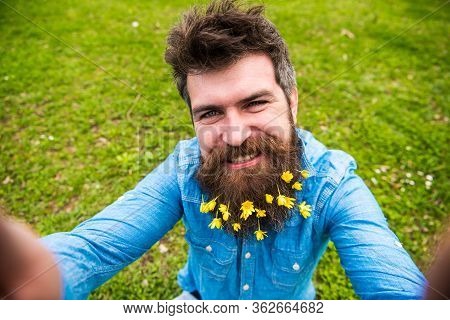 Hipster On Happy Face Taking Selfie Photo. Man With Beard Enjoys Spring, Green Meadow Background, De