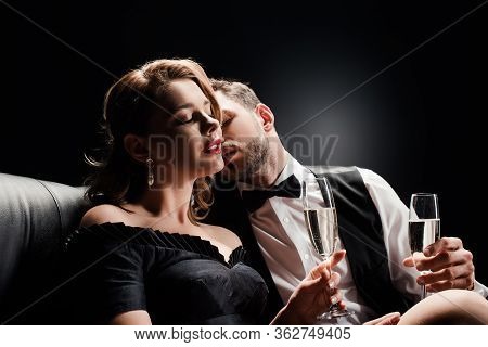 Elegant Man Kissing Seductive, Beautiful Woman Sitting With Closed Eyes On Black Background