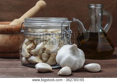 Still Life In Horizontal View Of An Oil Pourer With Olive Oil, Three Head Of Garlic And Leaves Of Pa