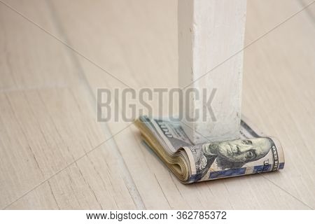 A Pack Of American Dollars Under A Table Leg On A Gray Floor Background. Depreciation Of Money, Econ