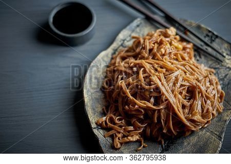 Buckwheat Noodle With Teriaki Sauce. Asian Dish. With Wooden Sticks. On A Clay Plate And A Gray Back