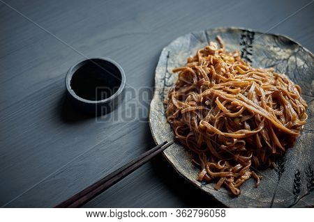 Buckwheat Noodle With Teriaki Sauce. Asian Dish. With Wooden Sticks. On A Clay Plate And A Gray Back