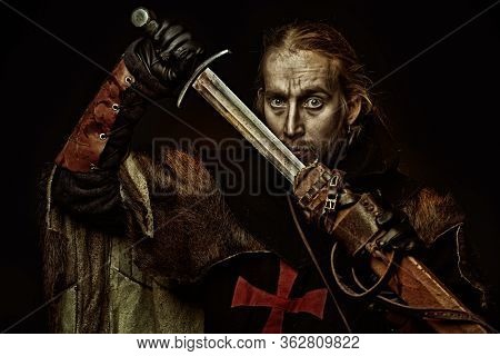 Portrait of a medieval knight in armour and with a sword over black background. Knight Templar. Historical reenactment.