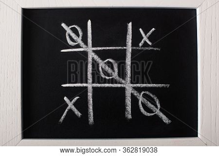 Top View Of Tic Tac Toe Game On Blackboard With Crossed Out Row On Naughts