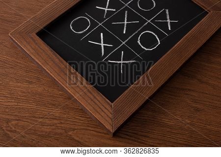 Tic Tac Toe Game On Blackboard With Chalk Grid, Naughts And Crosses On Wooden Surface