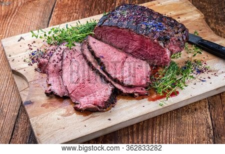 Traditional Commonwealth Sunday roast with sliced cold cuts roast beef with herbs and salt as closeup on a rustic wooden cutting board 