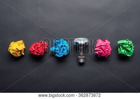 Lightbulb And Crumpled Colorful Paper Balls On Black Background. Successful Solution Of Problem. Ide