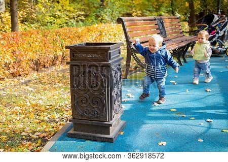 A Little Cute Baby In Blue Clothes Goes To A Street Bin In A Park And Throws Garbage There And Laugh