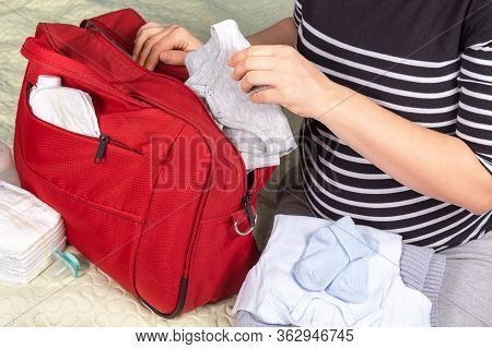 Unrecognizible Pregnant Caucasian Woman In Striped T-shirt Packing Big Red Diaper Bag To Maternity H