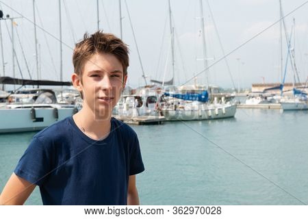 Portrait of teen boy over aquamarine water withsailing ships in port of Syracuse, Sicily. Boats and sea. Sailing vessels drop anchor in a quiet bay