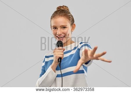 music and people concept - smiling teenage girl in pullover with microphone singing over grey background