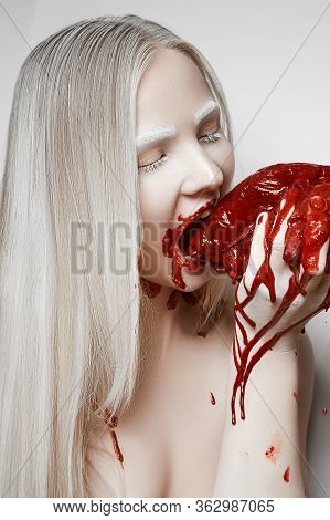 Young Blonde Girl With White Eyebrows Bites A Large Piece Of Bloody Meat
