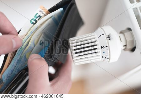 Close-up View Of Person Holding Wallet With Cash Next To Turned Down Thermostat On Radiator, Rising 