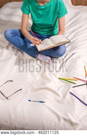 A Girl In A Green T - Shirt And Blue Jeans Is Sitting On The Bed And Writing In A Notebook , Colored