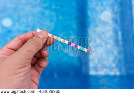 Hand With Measuring Pool Strips To Check Water Quality In A Swimming Pool