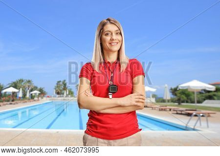Female swimming coach with a wistle and stopwatch posing next to an outdoor swimming pool