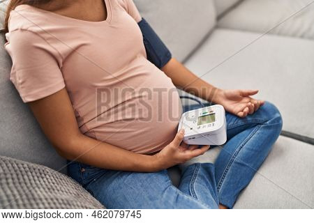 Young latin woman pregnant using tensiometer at home