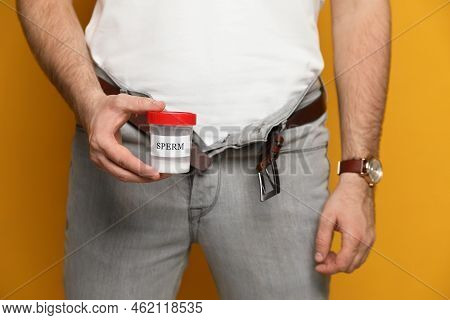 Donor With Unzipped Pants Holding Container Of Sperm On Yellow Background, Closeup