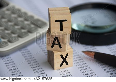 Tax Word On Wooden Blocks With Calculator, Pen, Magnifying Glass And Data Analysis Background. Tax C