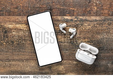 Mockup Mobile Phone With White Blank Screen. White Wireless Bluetooth Headphones And Charging Case A