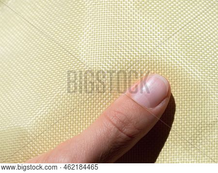 Finger On Bulletproof Material Aramid. Shining Aramid Kevlar Background. Yellow Kevlar Texture And P