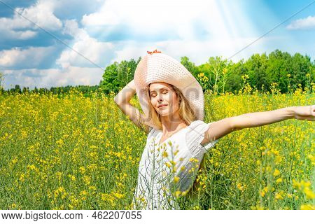 Beautiful Girl In Wide-brimmed Hat In A Flowering Field With White Dress. Sunbeams, Glare, Light Lea