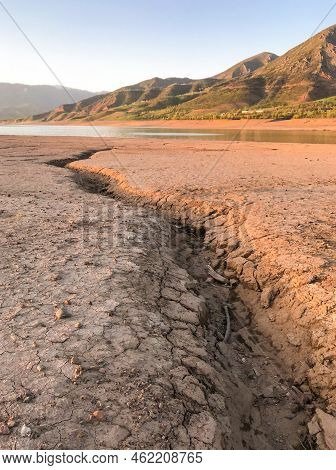 Beautiful Landscape With Setting Sun: Mountains, Lake, Cracked Earth With Stones -dried-up Riverbend