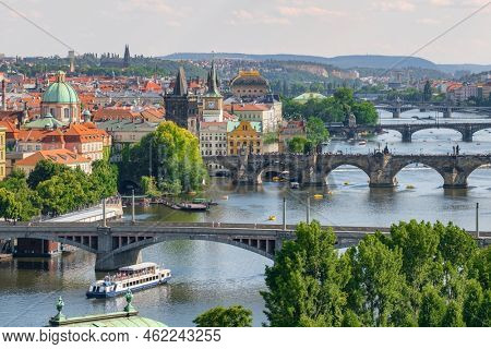 Prague cityscape in summer. Prague old town, Charles bridge and Vltava river, Czech Republic. View through tree leaves of Prague old bridges over the Vltava river at sunny day Czech capital city.
