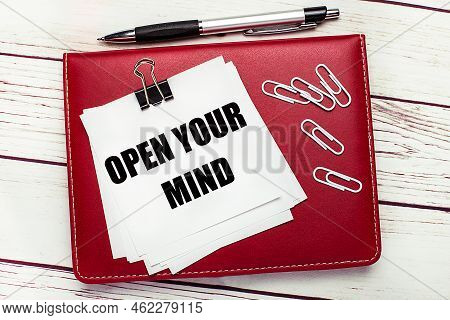 On A Light Wooden Background, A Burgundy Pen And Notebook. On The Notebook Has White Paper Clips And