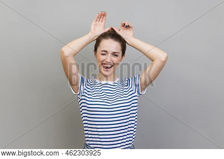 Portrait Of Playful Woman Wearing Striped T-shirt Making Funny Bunny Ears With Hands On Head, Childi