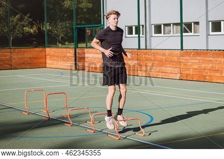 Blond Boy In Sportswear Jumps Over Red Hurdles To Improve Lower Body Dynamics. Plyometric Training I