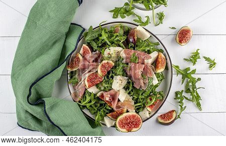 Salad With Arugula , Figs, Prosciutto And Mozzarella And Green Napkin On A Wooden Background