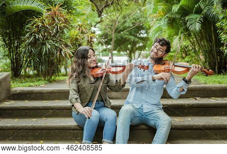 Portrait Of Two Young Violists Playing Violin Sitting On Stairs Outside. Portrait Of Smiling Violini