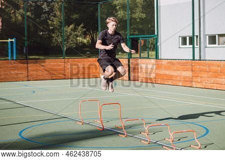 Blond Boy In Sportswear Jumps Over Red Obstacles To Improve Lower Body Dynamics. Plyometric Training
